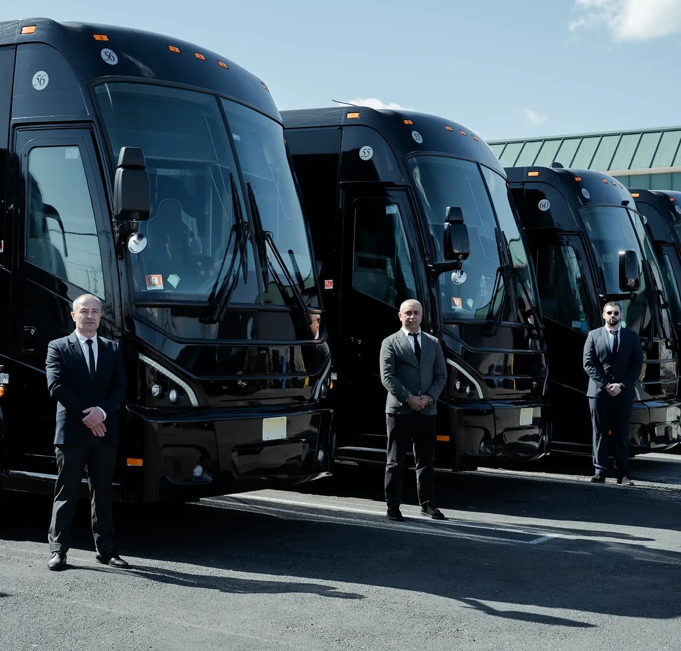Chauffeurs standing at attention beside black motorcoaches