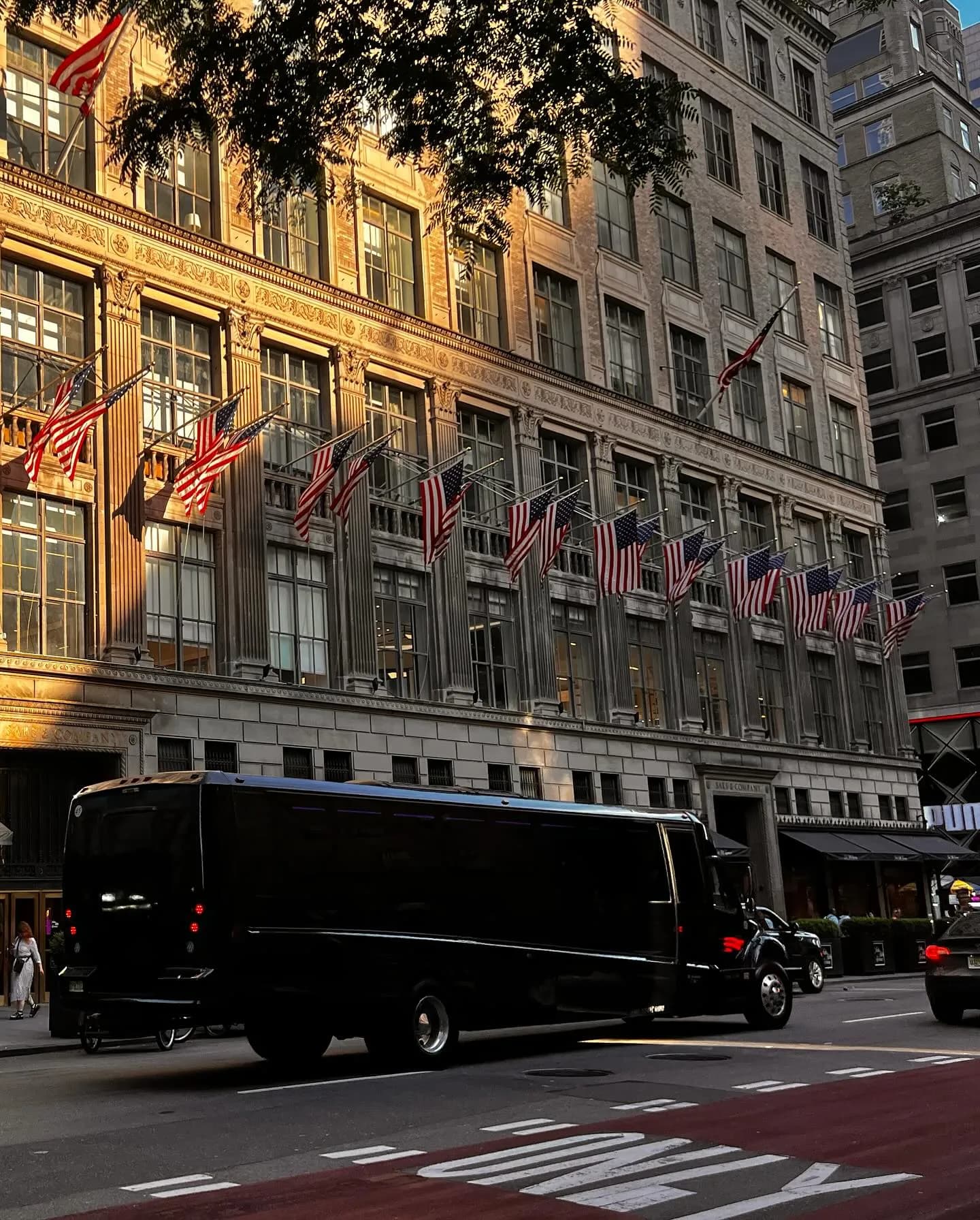 Black coach bus outside the flag-lined Saks Fifth Avenue building