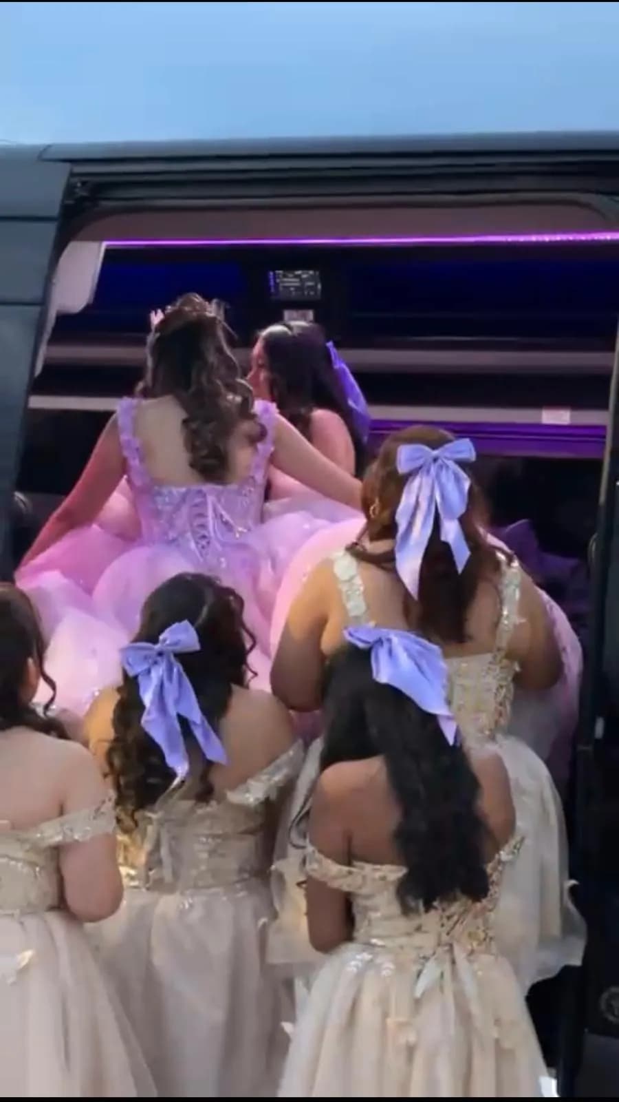 Quinceañera guests in formal gowns boarding a King & Queen Limo party bus with purple LED lighting.