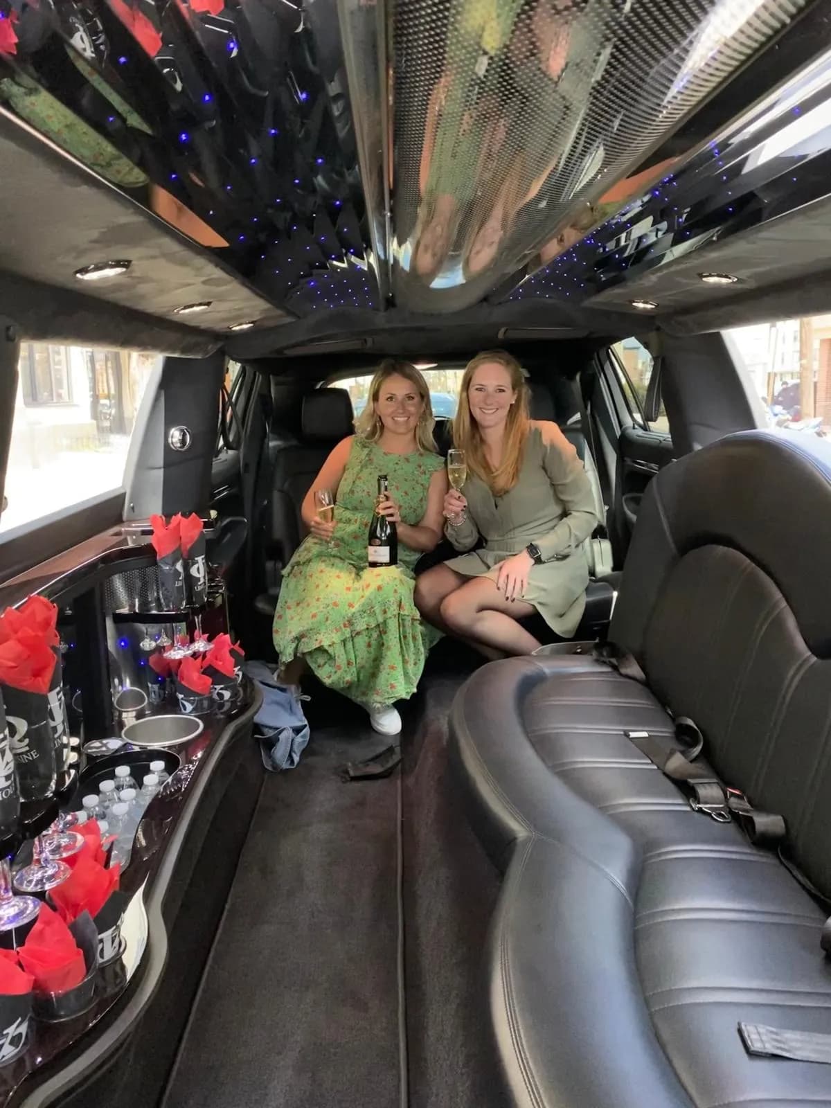 Two guests with champagne inside a stretch limousine dressed with red roses