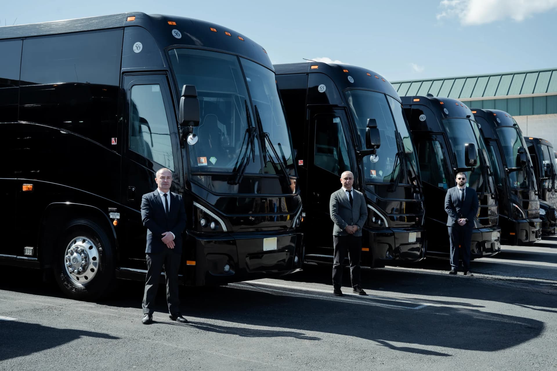 Three professional chauffeurs standing beside a lineup of King & Queen Limo 56-passenger motorcoaches in NYC.