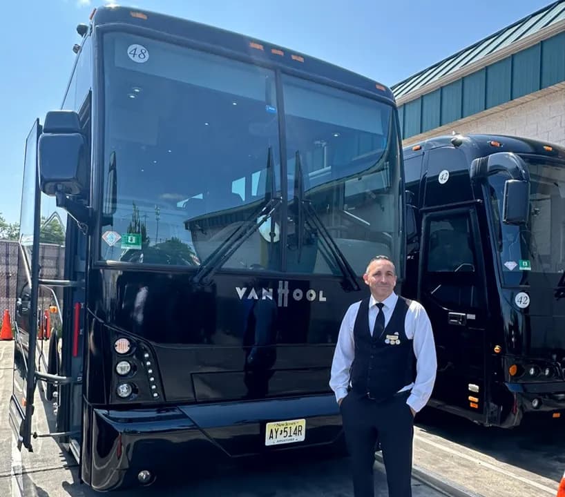 Chauffeur standing in front of a black Van Hool 56 passenger motorcoach