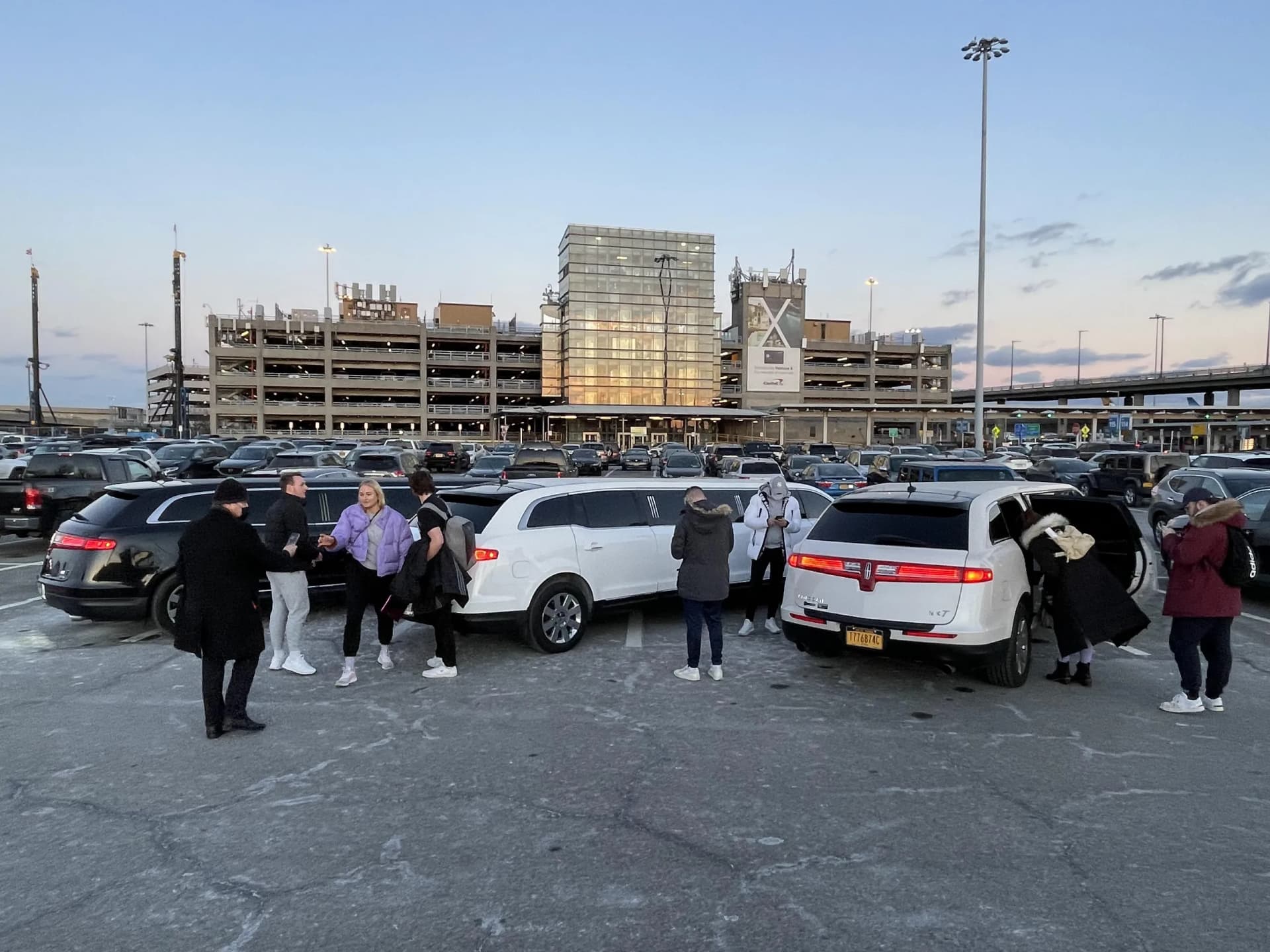 White and black Lincoln stretch limousines picking up passengers at a New York City airport at dusk.