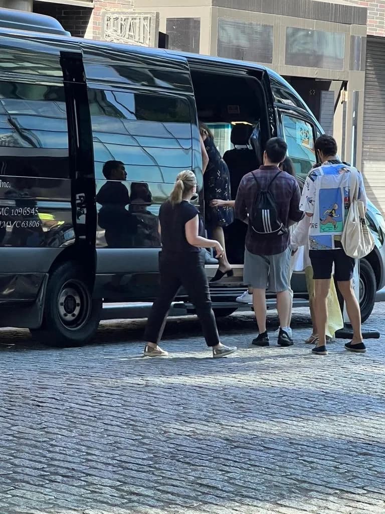 Passengers boarding a black Mercedes Sprinter van on a cobblestone street in Manhattan.