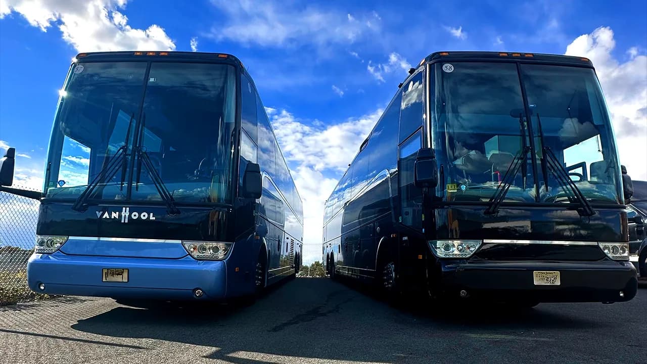 Two Van Hool coach buses with restrooms parked side by side under a blue sky