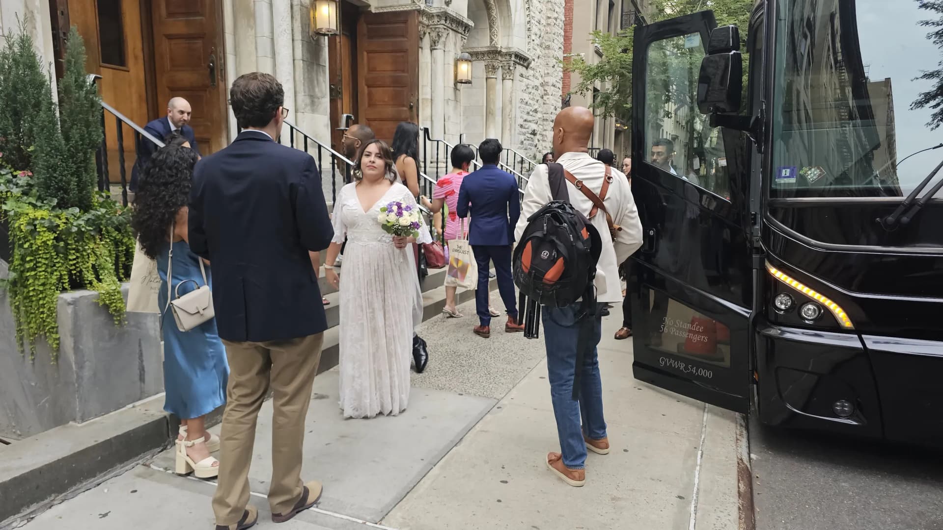Bride carrying her bouquet while boarding a 56-passenger wedding shuttle outside a Manhattan church.