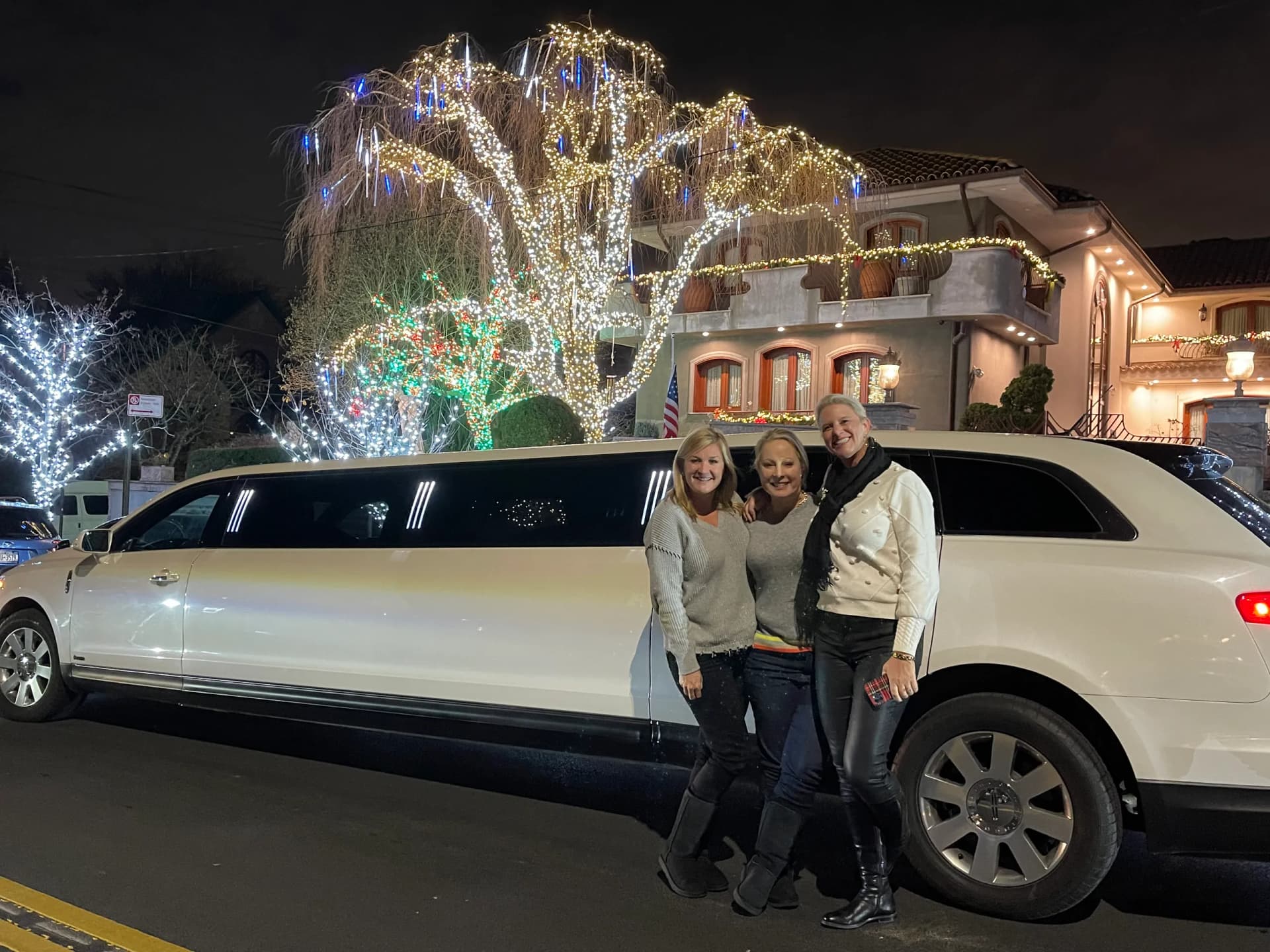 Three friends with a white limousine on the Dyker Heights Christmas lights tour