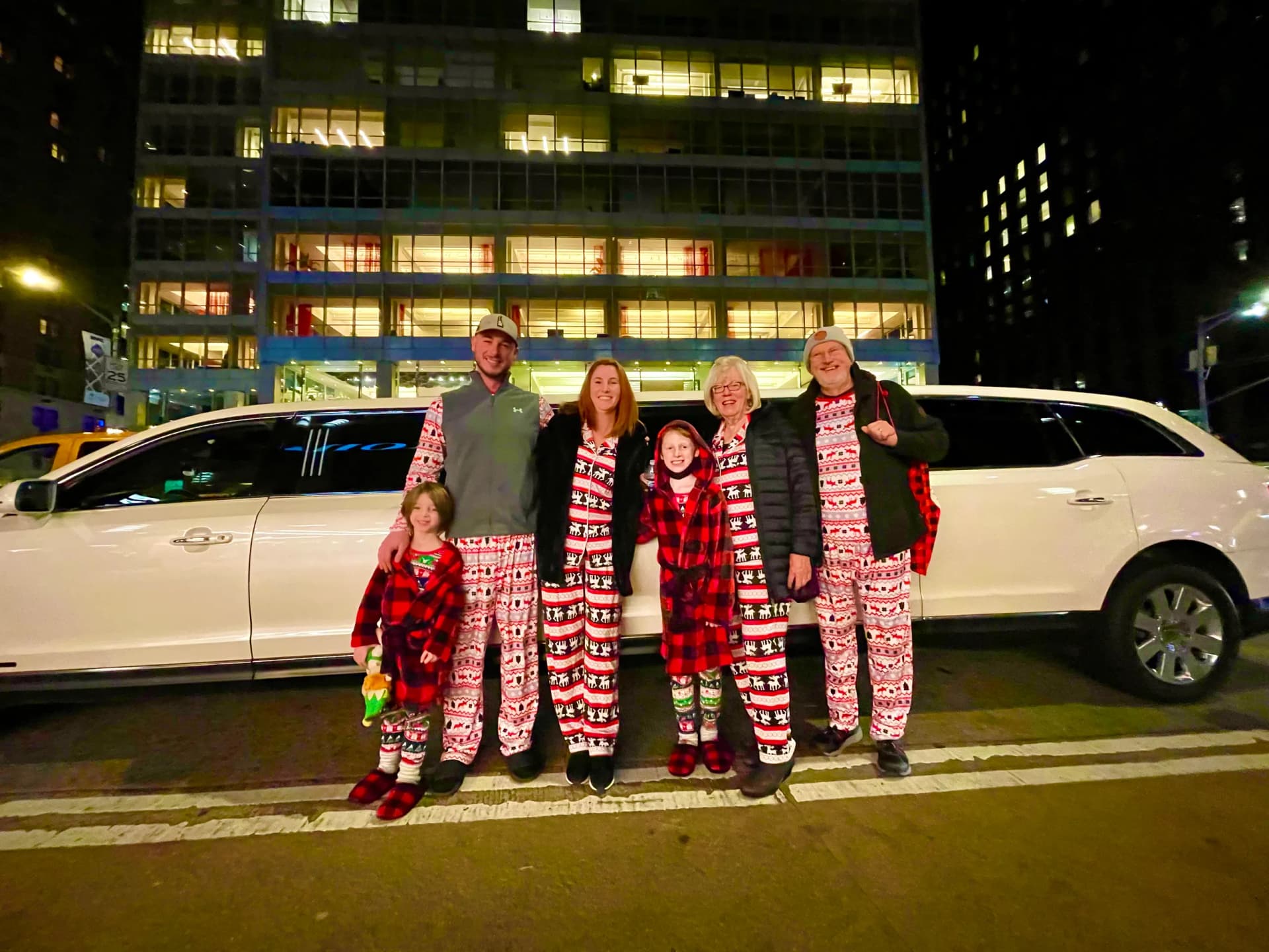 Family in matching Christmas pajamas beside a white limousine in Midtown