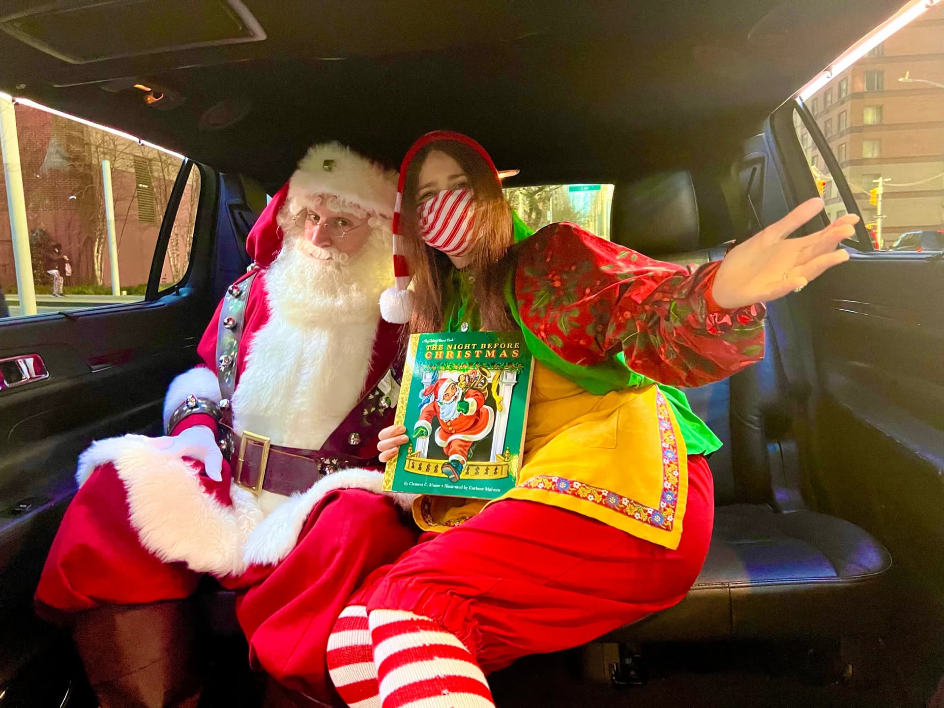 Santa and elf reading The Night Before Christmas in the back of an SUV