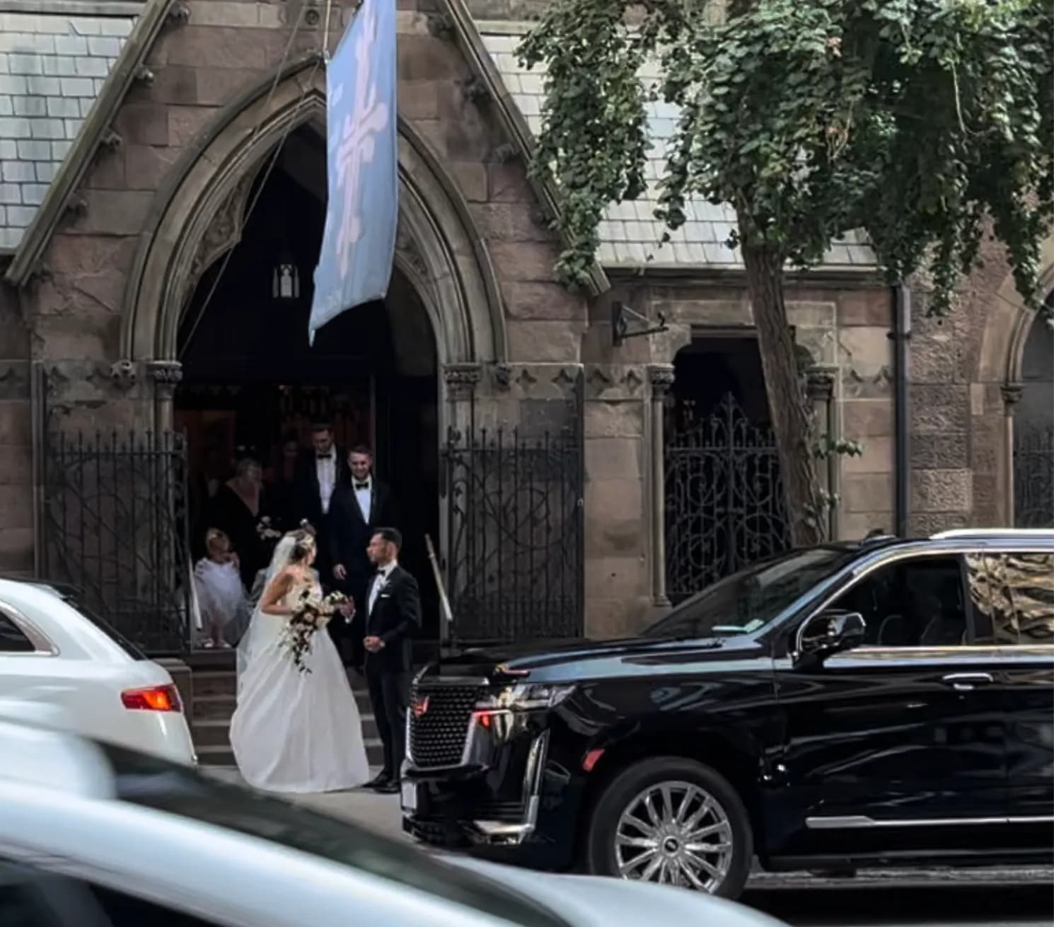 Bride and groom leaving a Manhattan church with a black Cadillac Escalade waiting at the curb.