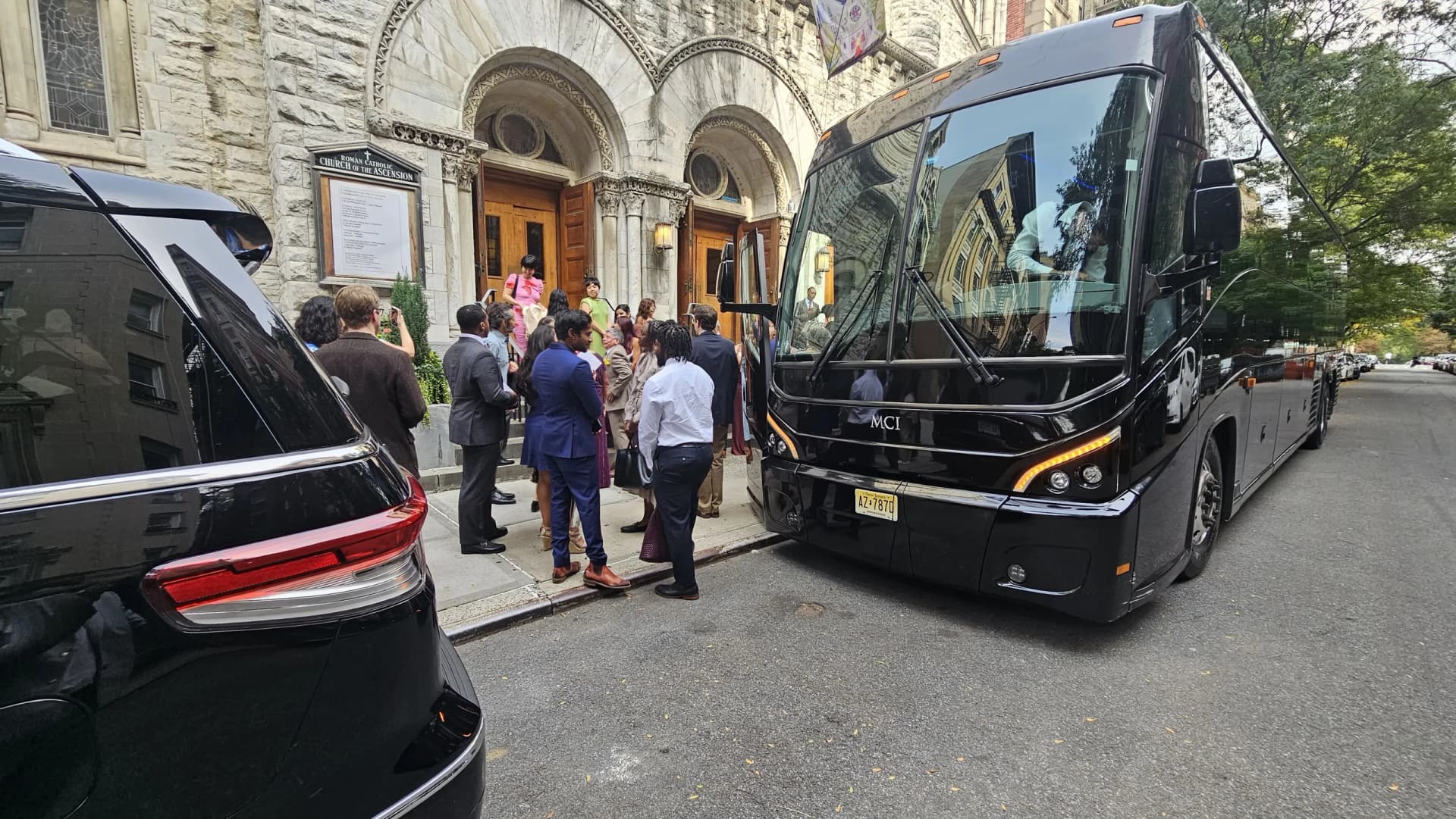 Wedding guests boarding a black MCI motorcoach shuttle outside the Church of the Ascension in New York City.