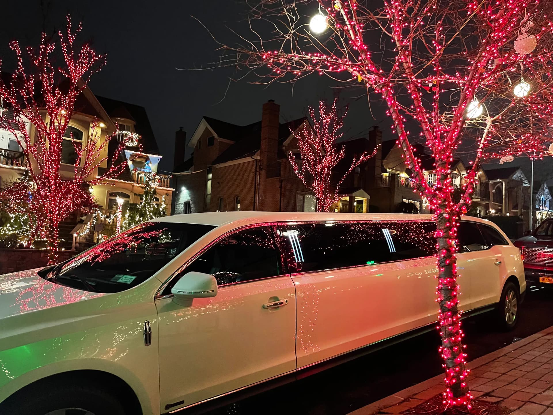 White stretch limousine parked under trees wrapped in red Christmas lights