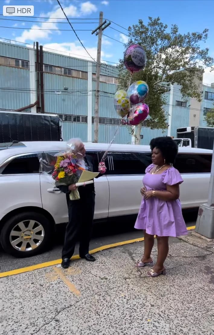 Chauffeur presenting flowers and balloons beside a white stretch limousine for a birthday surprise