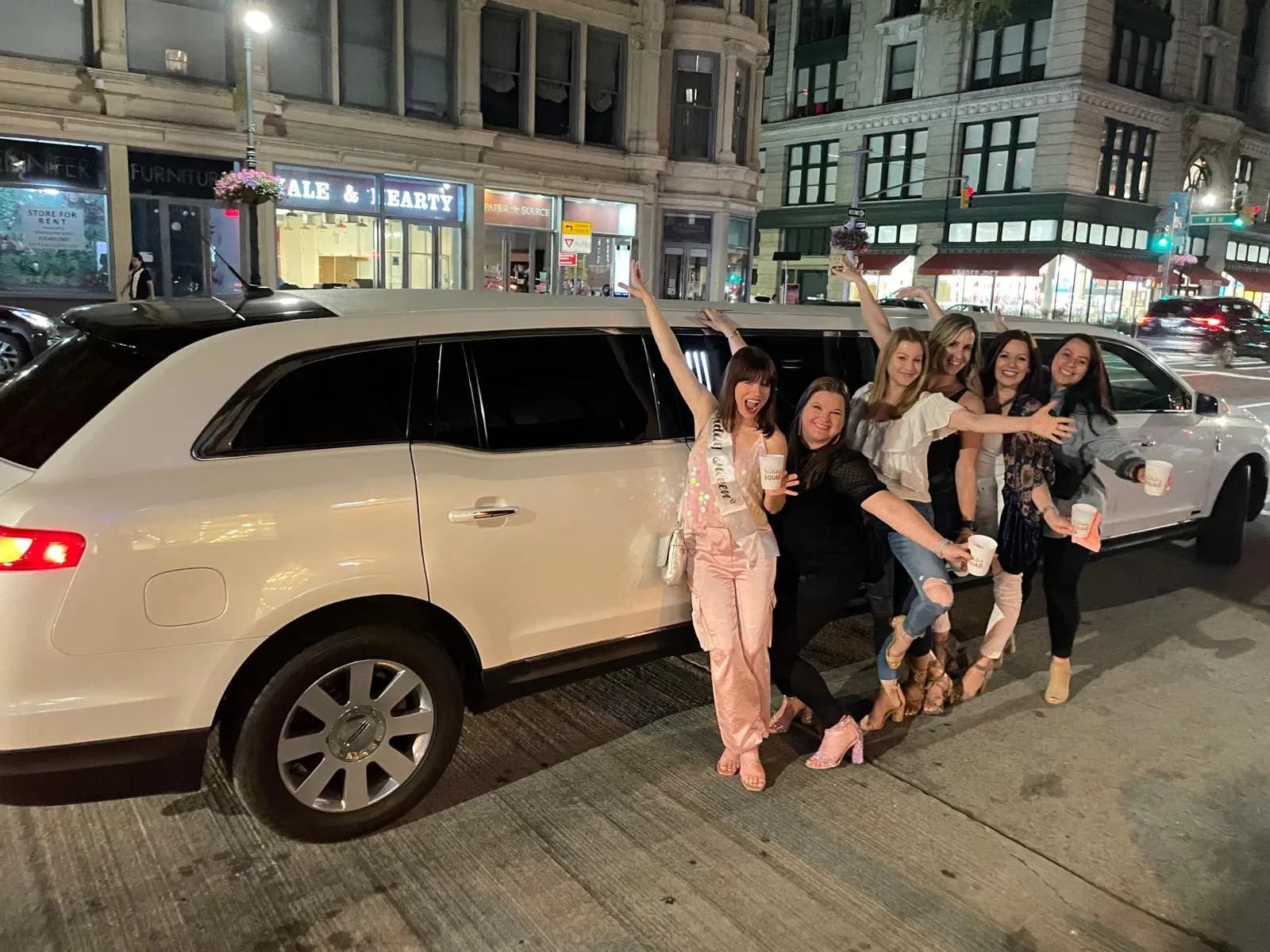 Friends posing beside a white Lincoln stretch limousine on a night out
