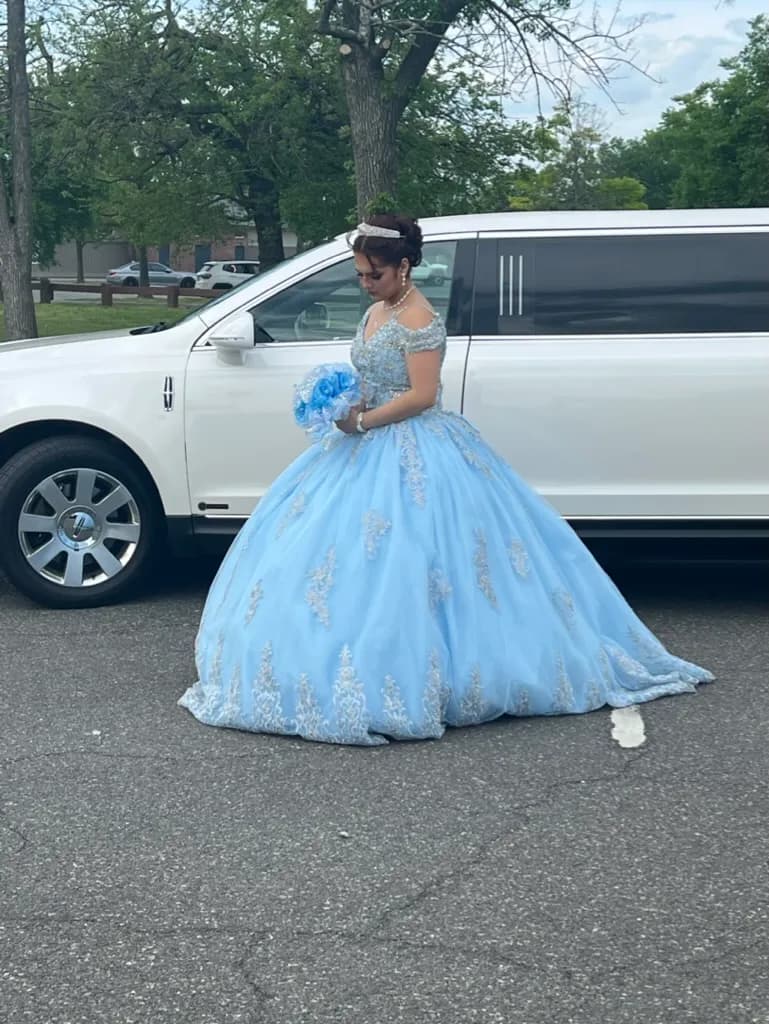 Quinceanera in a light blue gown with her bouquet beside a white stretch limousine