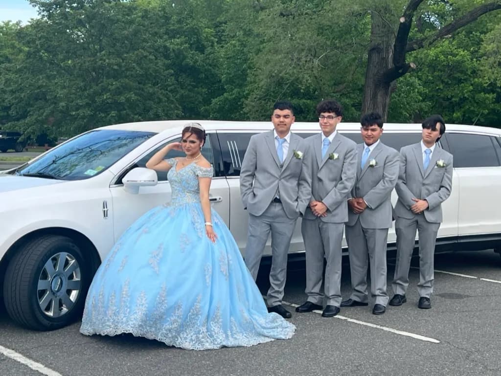 Sweet 16 celebrant in a blue gown with her court beside a white stretch limousine