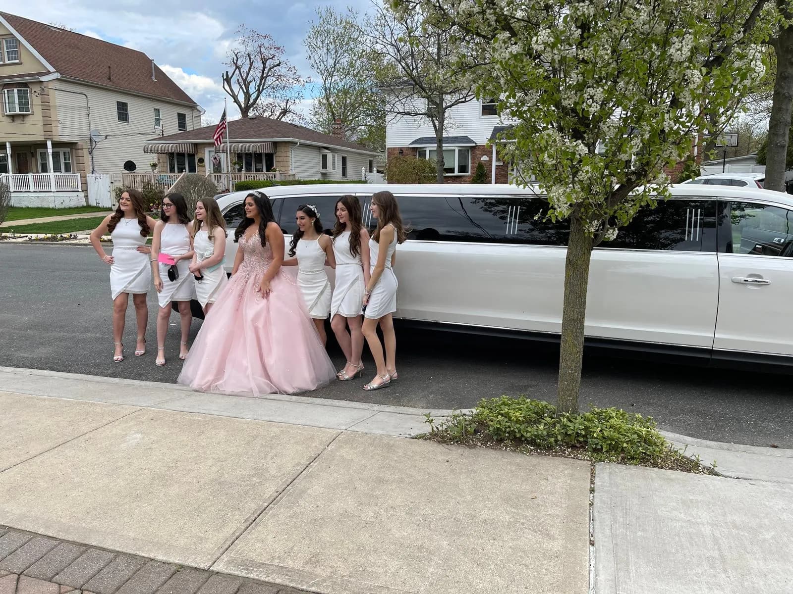 Sweet 16 celebrant in a pink gown with friends beside a white stretch limousine