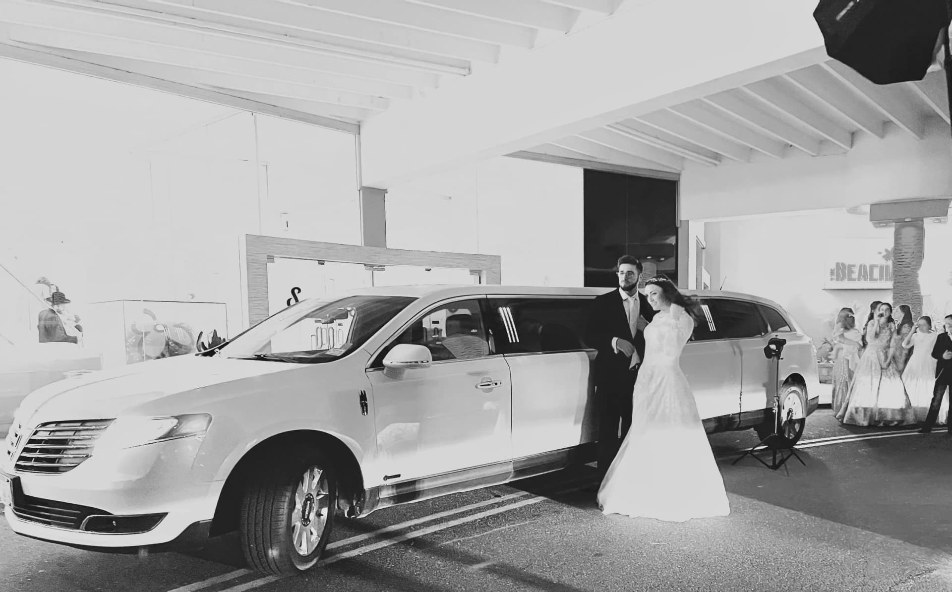 Bride and groom beside a white Lincoln limousine at the venue, black and white photo