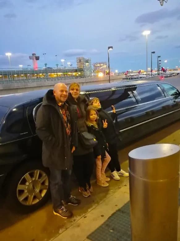 Family beside a black stretch limousine at the JFK terminal in the evening