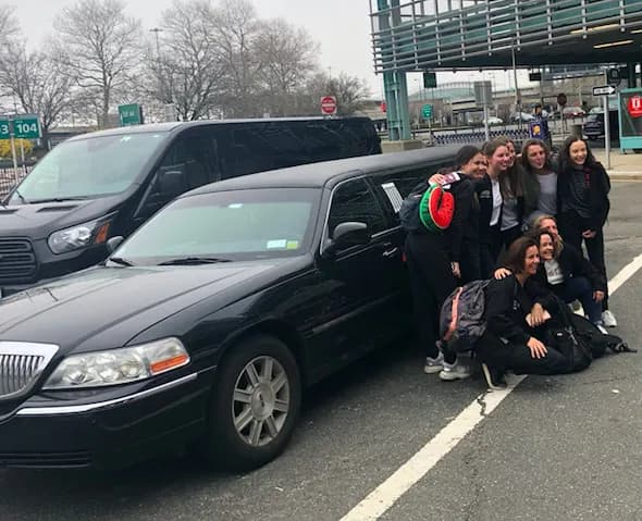 Group posing with a black Lincoln stretch limousine at the airport