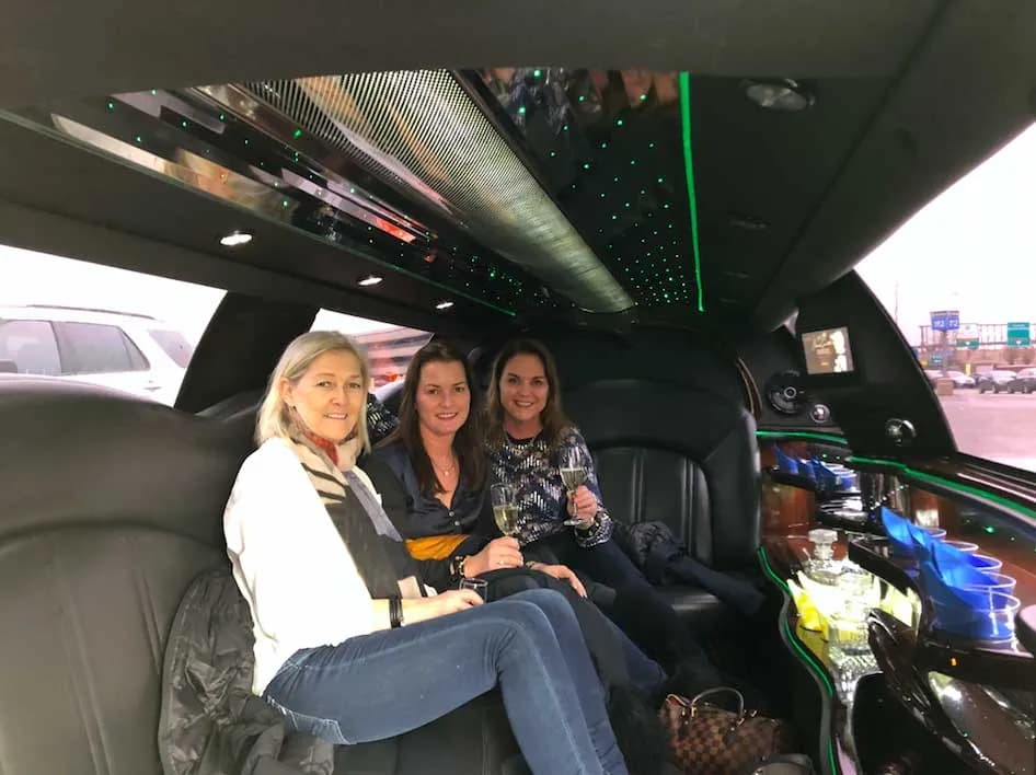 Three friends with wine glasses inside a stretch limousine on a daytime tour