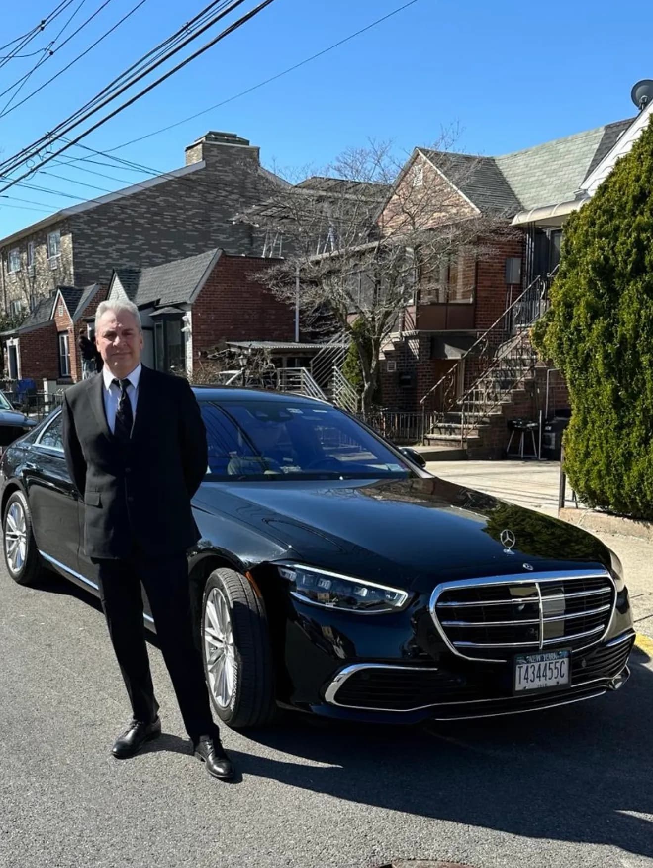 Chauffeur standing with a black Mercedes S-Class on a residential Queens street