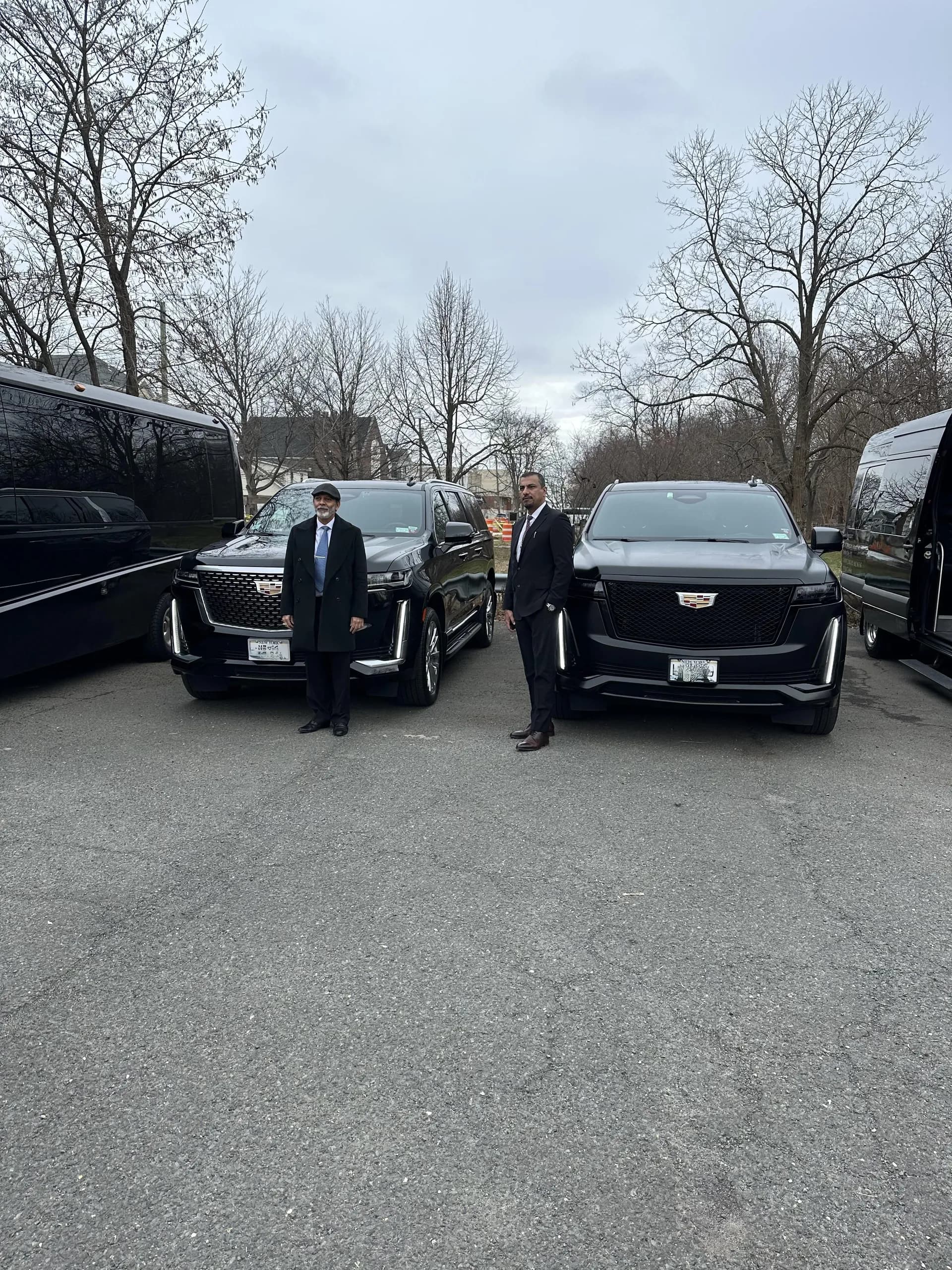 Two chauffeurs standing with black Cadillac Escalades between Sprinter vans