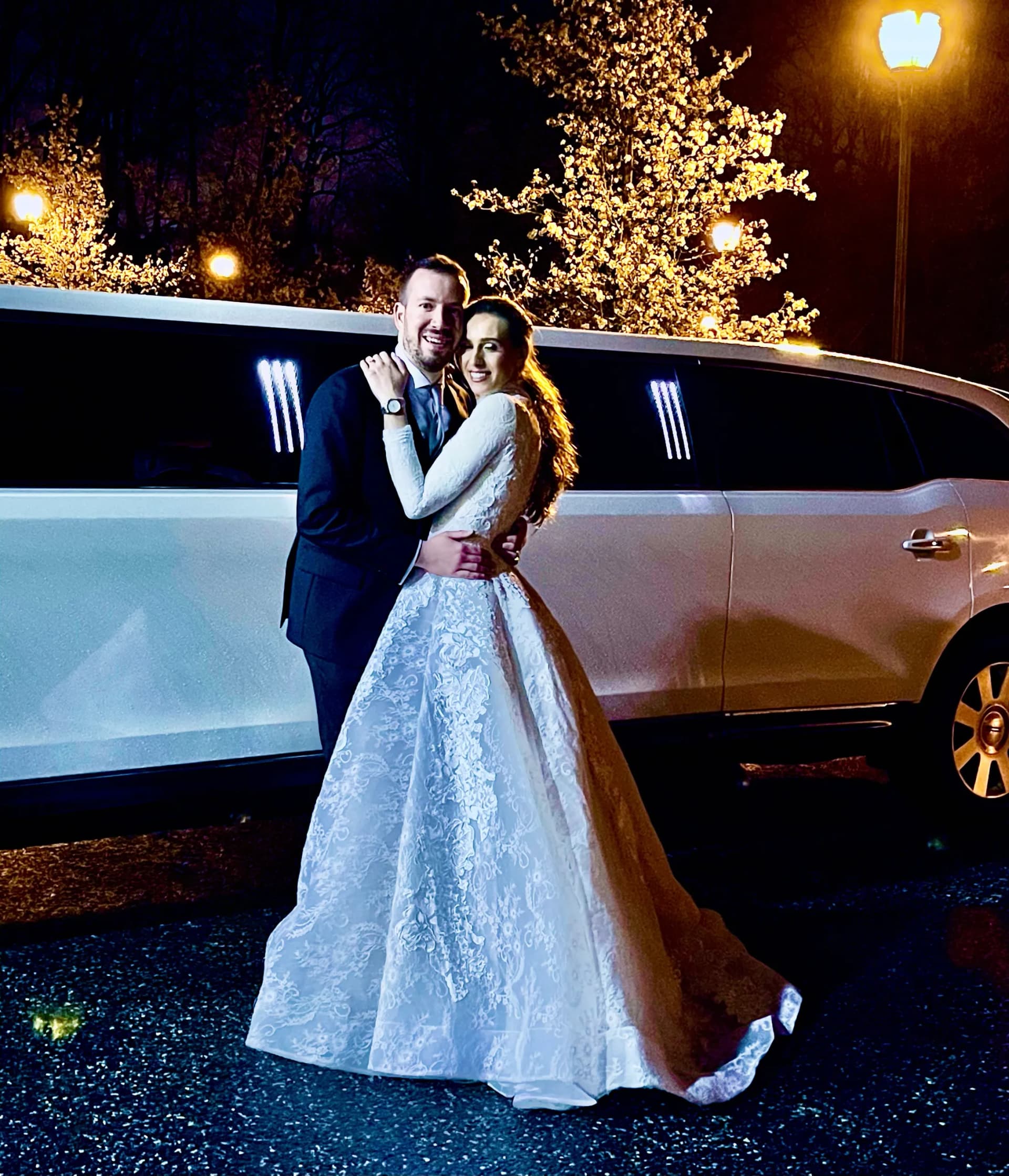 Couple embracing in front of a white limousine under evening lights