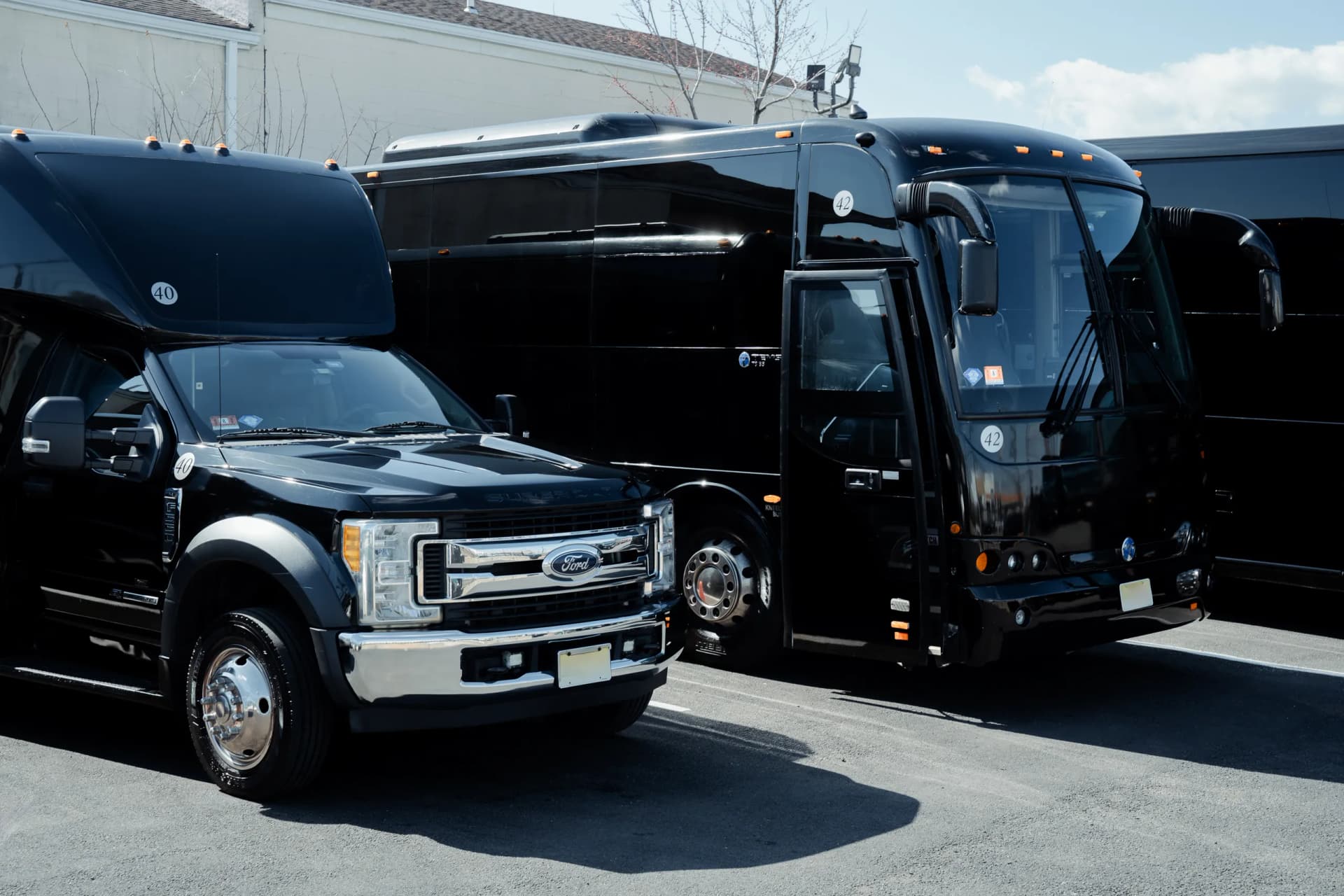 Ford F-550 mini bus parked beside a black coach bus in the yard