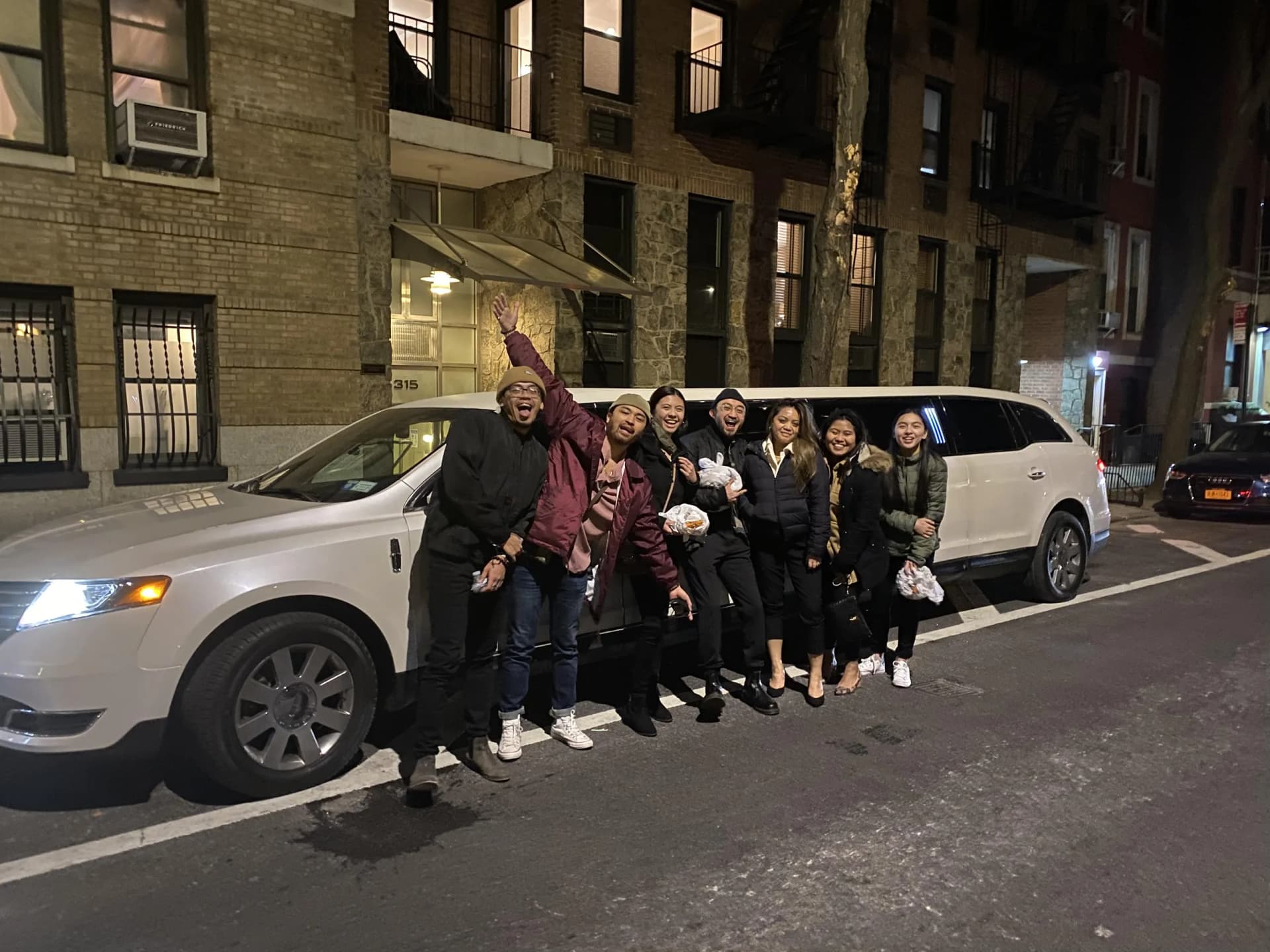 Friends cheering beside their white limousine on a night out