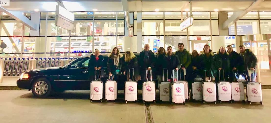 Tour group with matching suitcases beside a Lincoln limousine at the airport