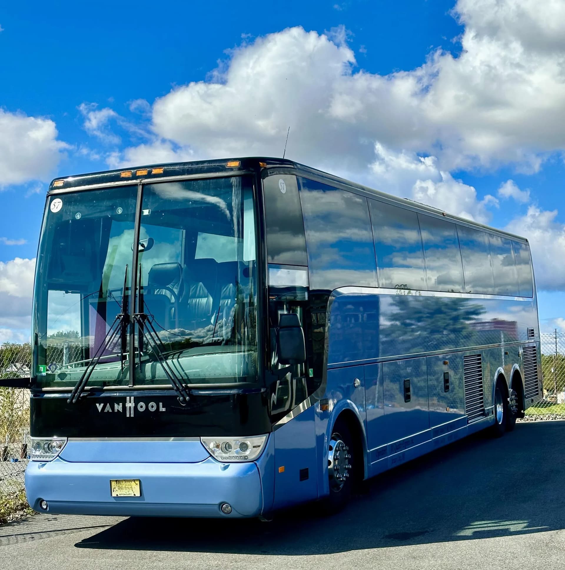 Van Hool coach bus in blue and black under summer clouds