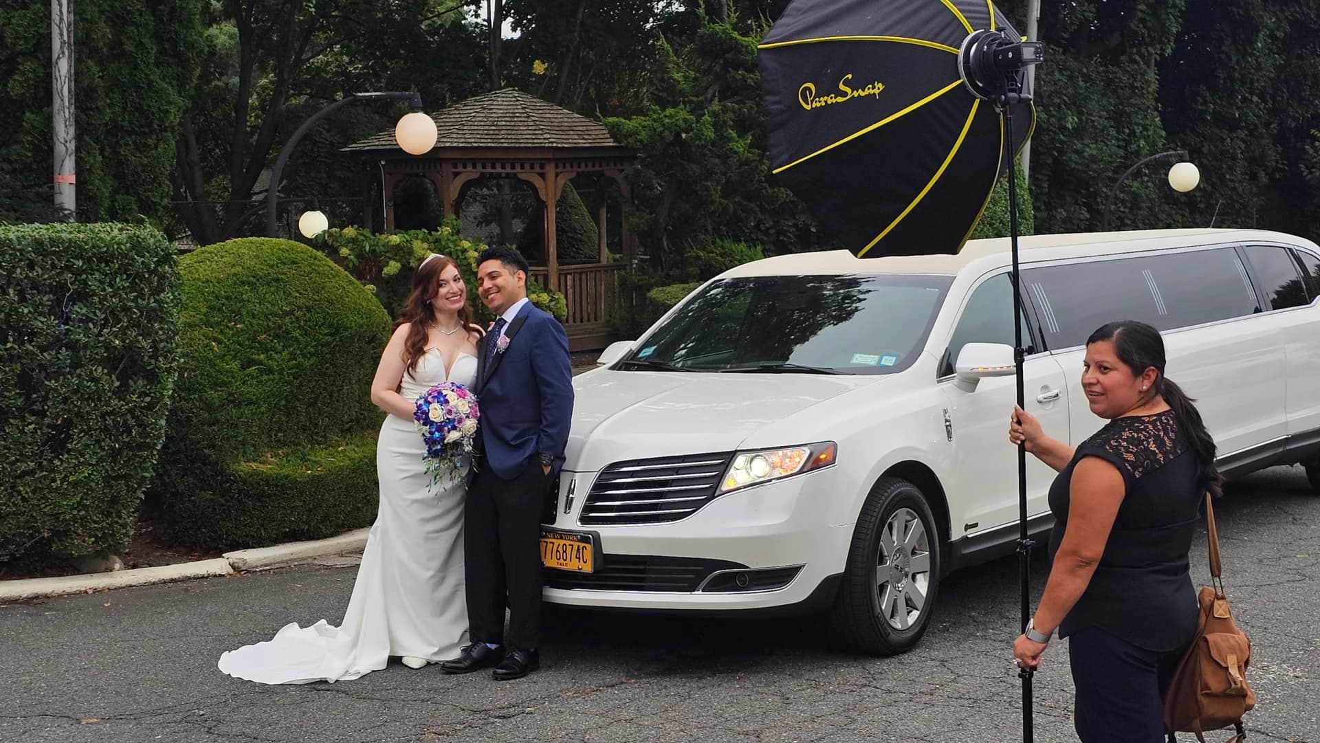 Newlyweds photographed with a white limousine beside a garden gazebo